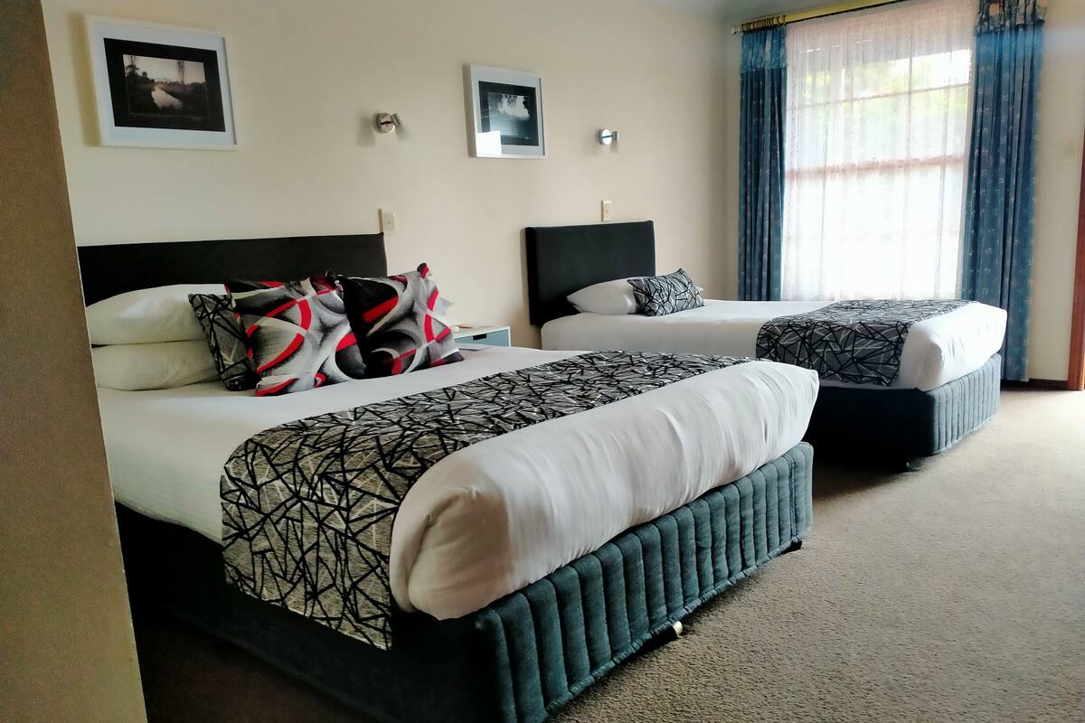 A hotel room with two beds, each with a headboard, a large window with curtains, and two framed pictures on the wall.