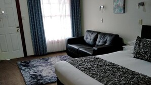 Een slaapkamer met een bed, een bank, een vloerkleed, een deur en gordijnen.