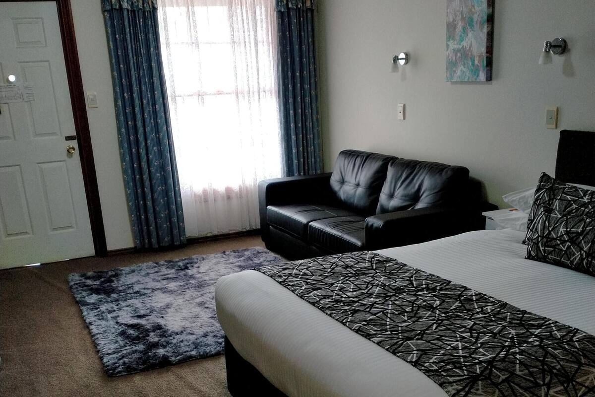 A bedroom with a bed, a sofa, a rug, a door, and curtains.