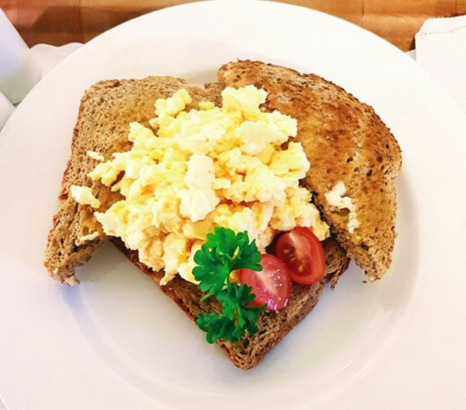 A sandwich with scrambled eggs, tomato slices, and parsley on a slice of whole grain bread.