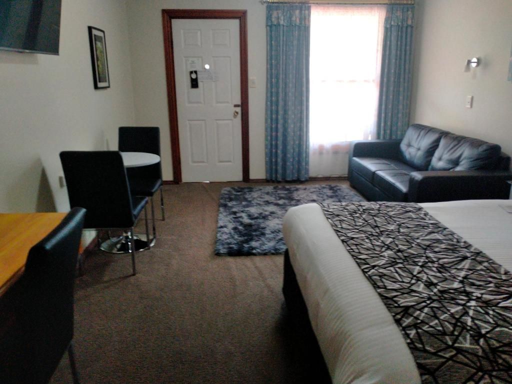 Habitación de hotel con cama, sofá, mesa de comedor con sillas, puerta y ventana con cortinas.