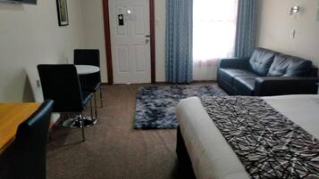 Habitación de hotel con cama, sofá, mesa de comedor con sillas, puerta y ventana con cortinas.