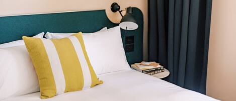 A neatly made bed with white and yellow striped pillows, a teal headboard, a black lamp, and a stack of books on a bedside table.