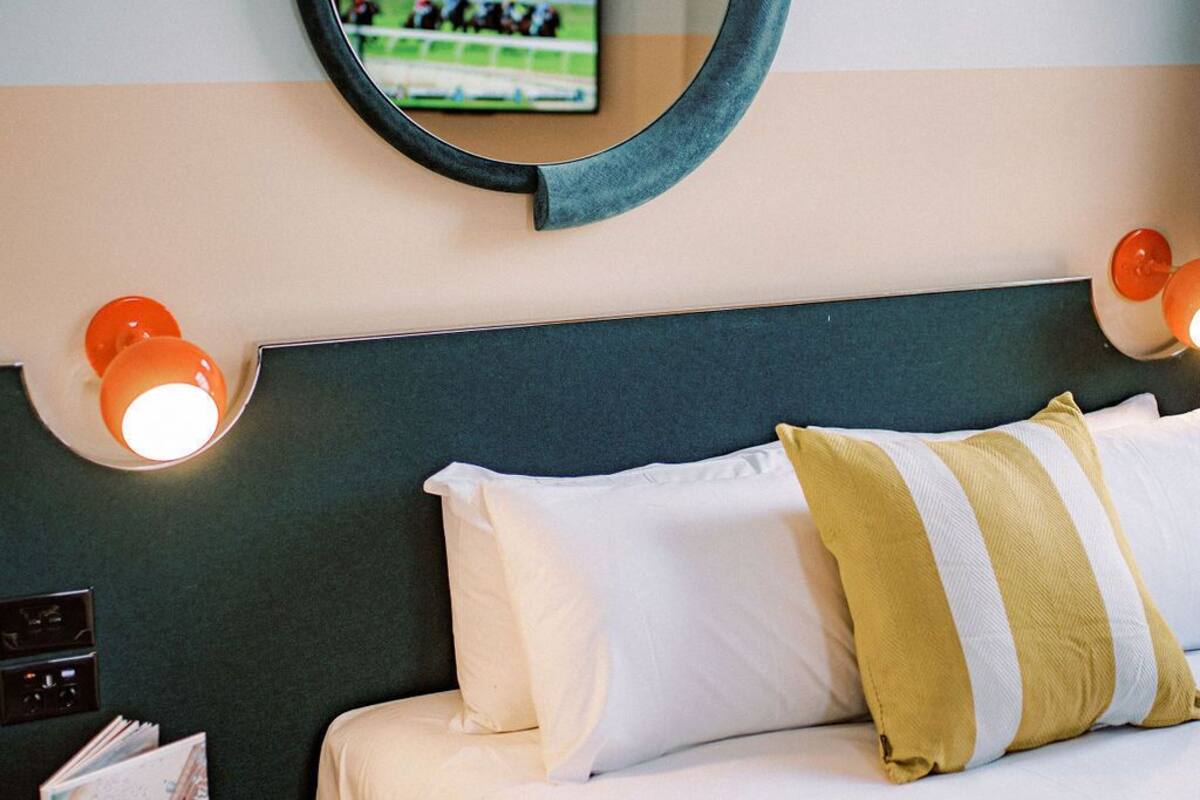 A hotel room with a bed, pillows, a round mirror, and a television on the wall.