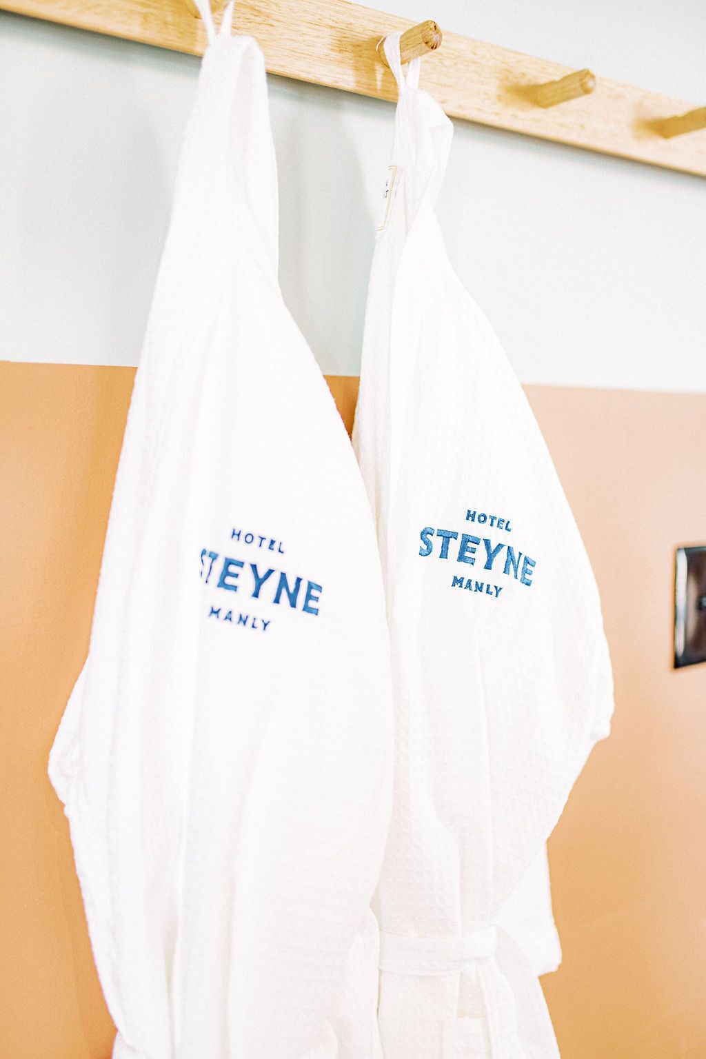 Two white towels hanging on a wooden rack with the text "HOTEL STEYNE MANLY" printed on them.