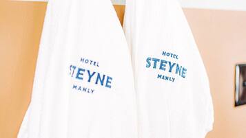 Two white towels hanging on a wooden rack with the text "HOTEL STEYNE MANLY" printed on them.