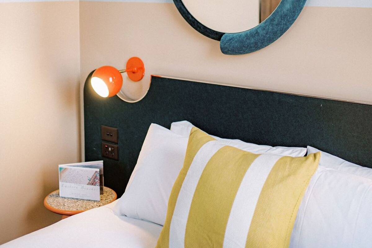 A hotel room with a bed, a round mirror, a bedside lamp, and a small table with a book.
