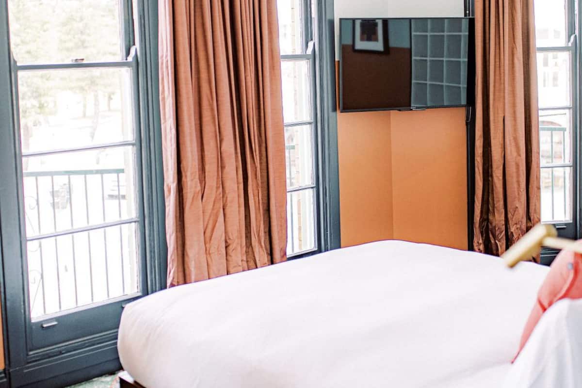 A bedroom with a bed, large windows with curtains, a headboard, and a tiled floor.