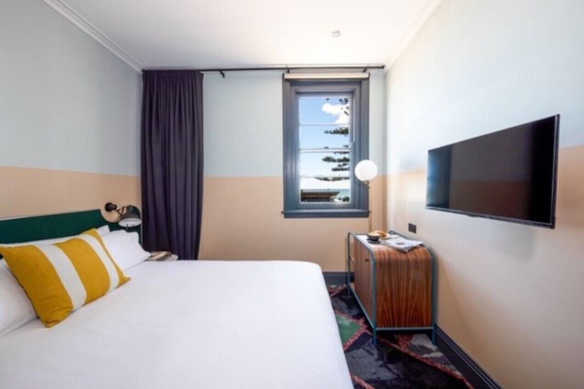 A hotel room with a bed, a television, a window with a view, and a small table with a lamp.