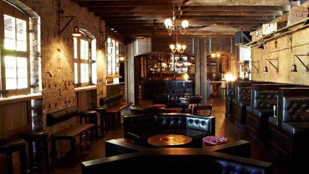 Un bar con vigas de madera, asientos de cuero y una barra central.