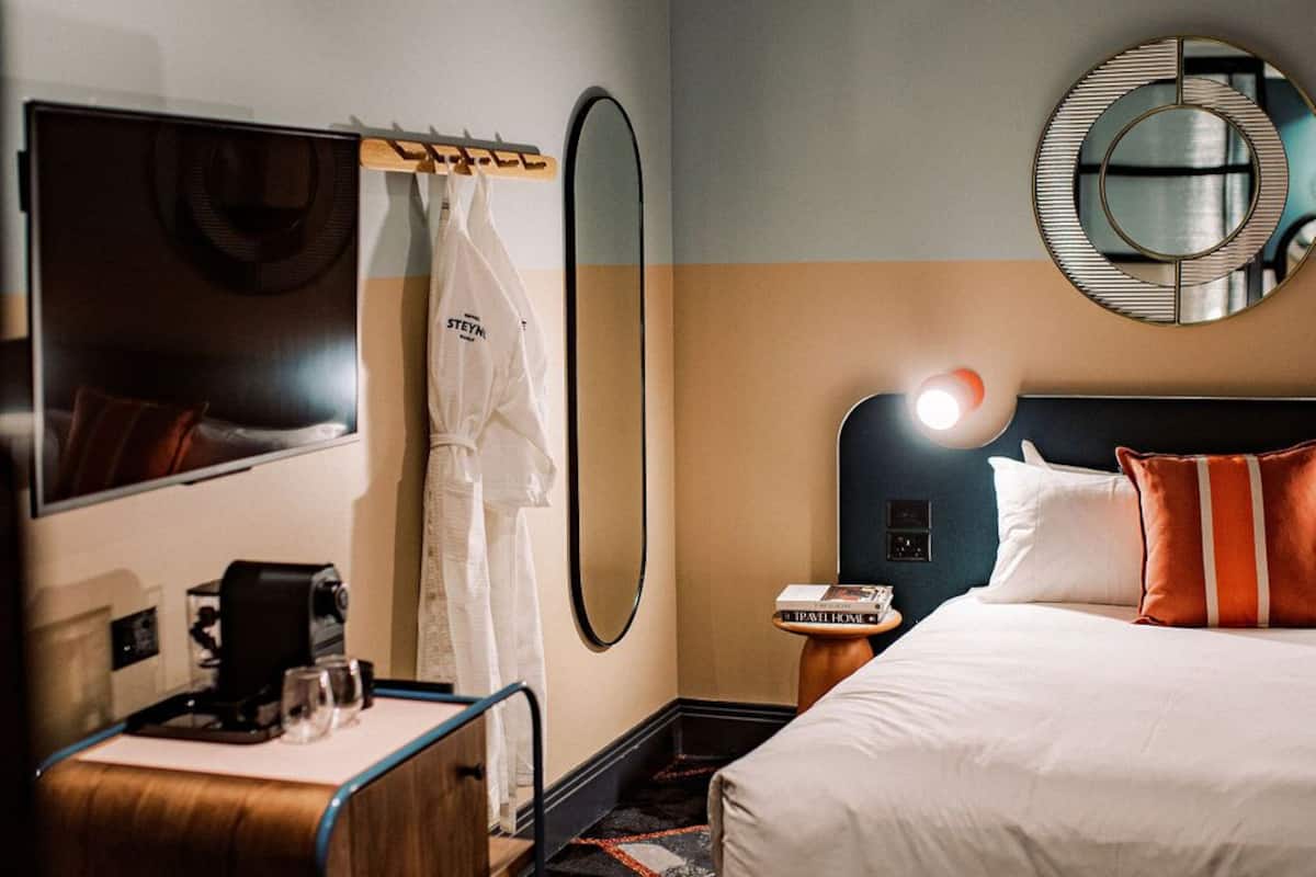 A hotel room with a bed, a bedside table with a lamp, a mirror, and a wardrobe.