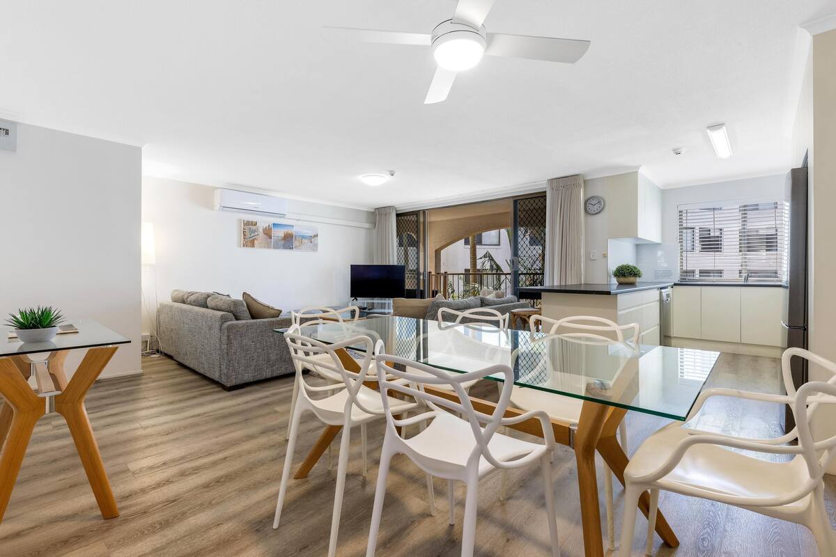 A modern kitchen with a dining area, a sofa, and a TV.