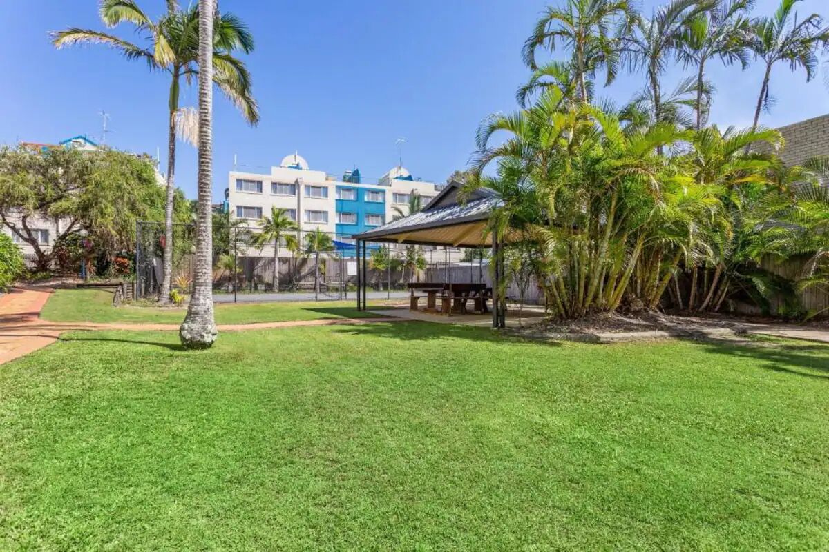 Zona verde bien cuidada con palmeras y un espacio de estar cubierto, probablemente parte de un hotel o resort.