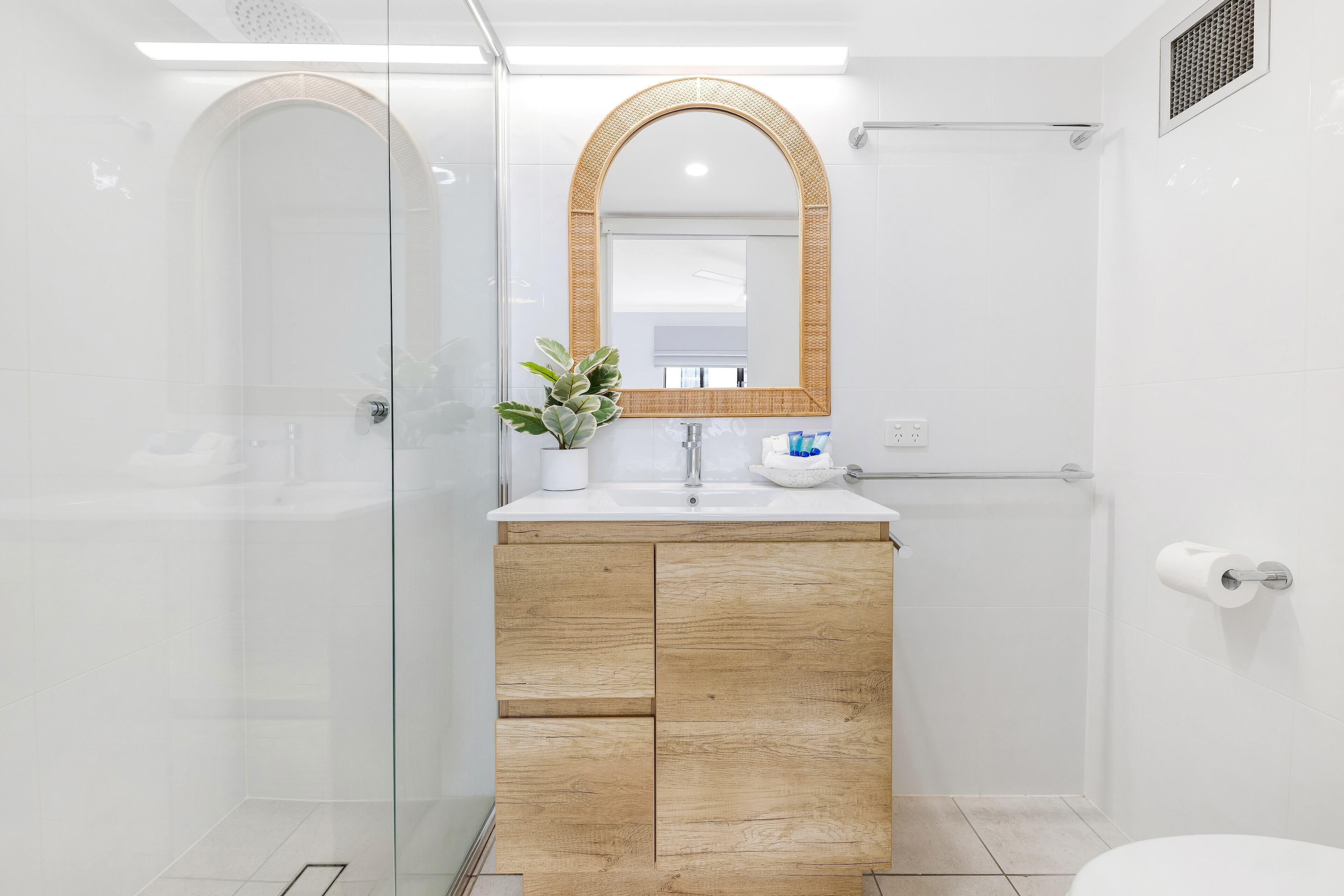 A modern bathroom with a glass shower enclosure, a wooden vanity, a large mirror, and a toilet.