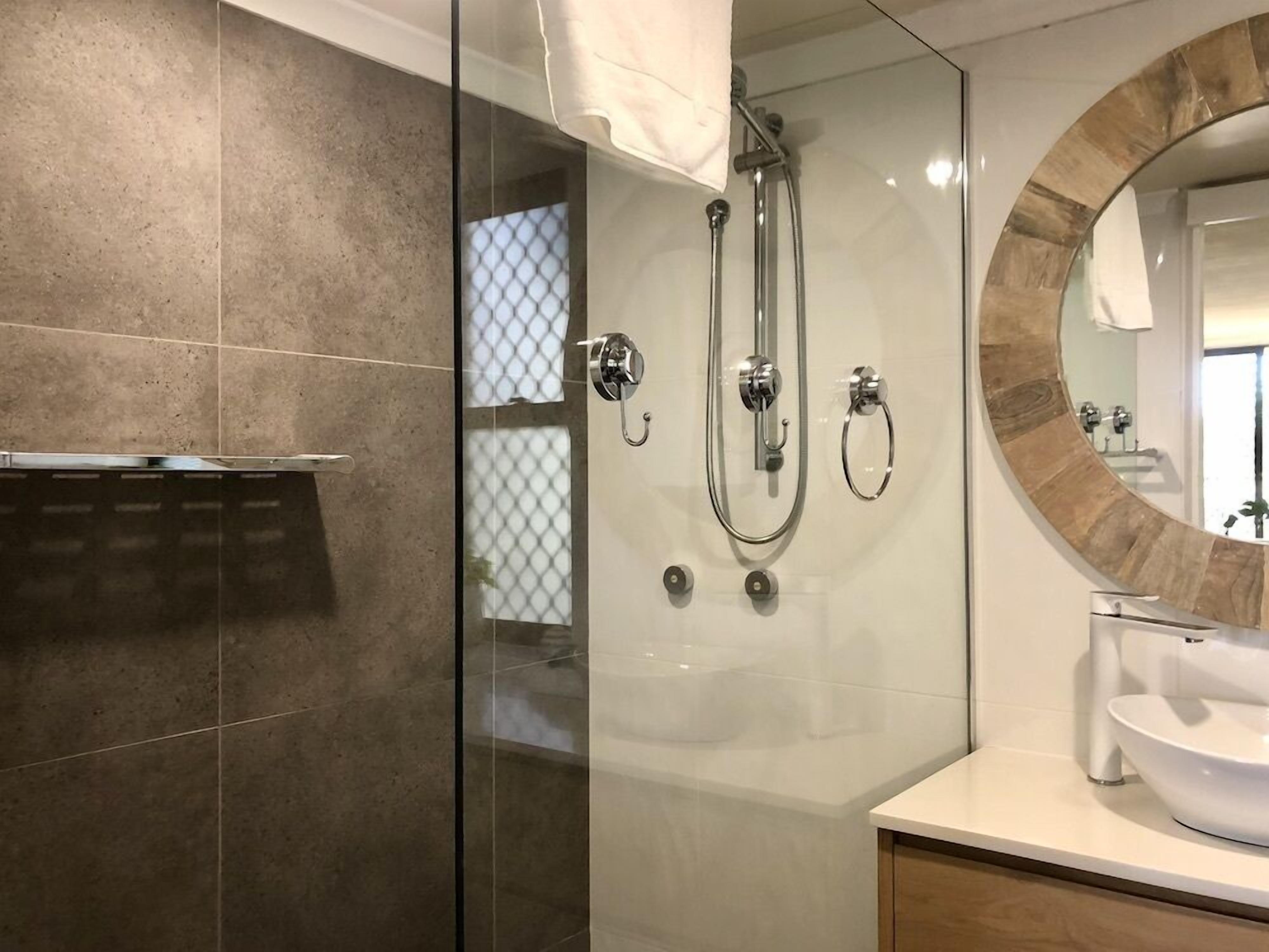 A modern bathroom with a glass-enclosed shower, a round mirror, and a white sink.