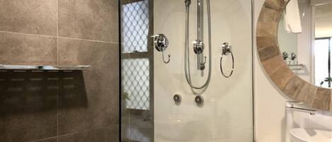 A modern bathroom with a glass-enclosed shower, a round mirror, and a white sink.