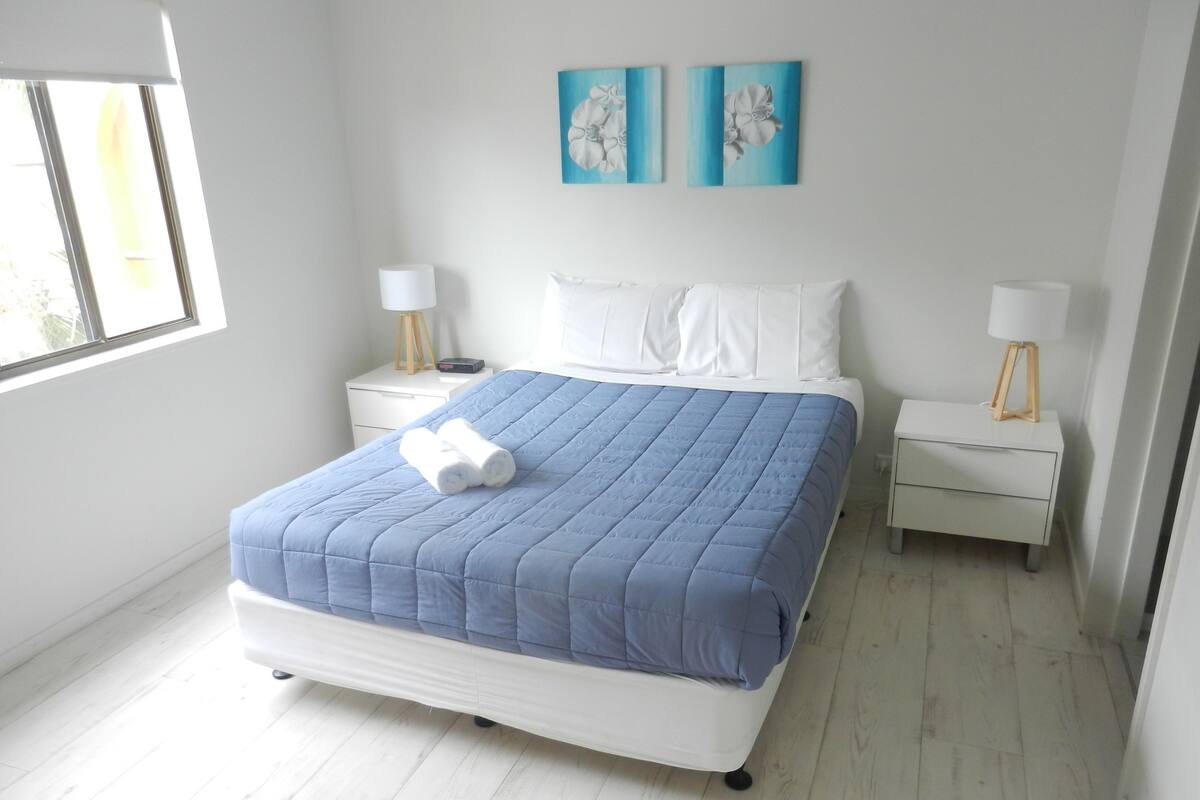 A bedroom with a bed, two nightstands, a window, and two wall art pieces.