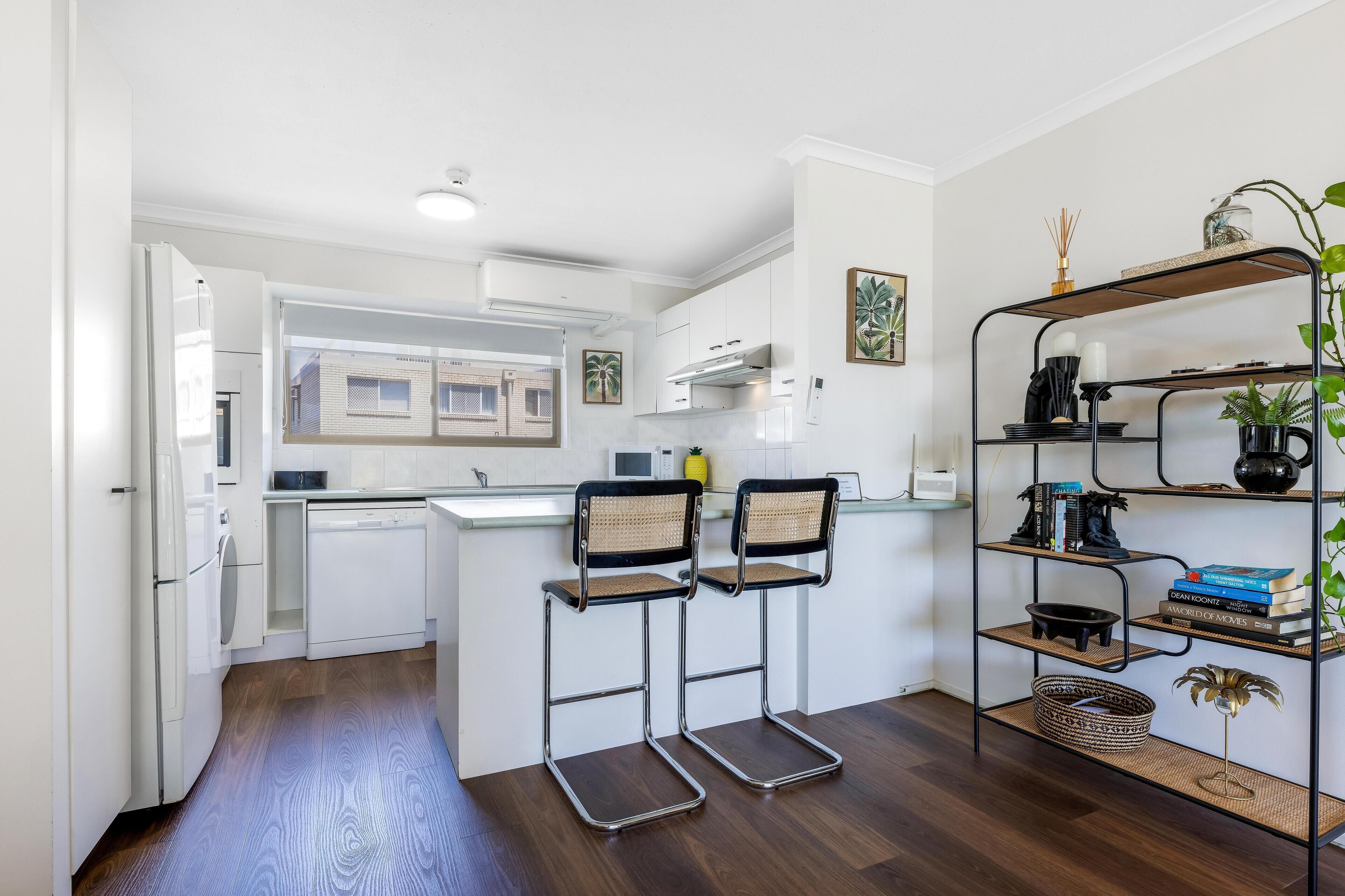 Una cocina moderna con armarios blancos, microondas integrado y ventana con vista a una zona residencial.
