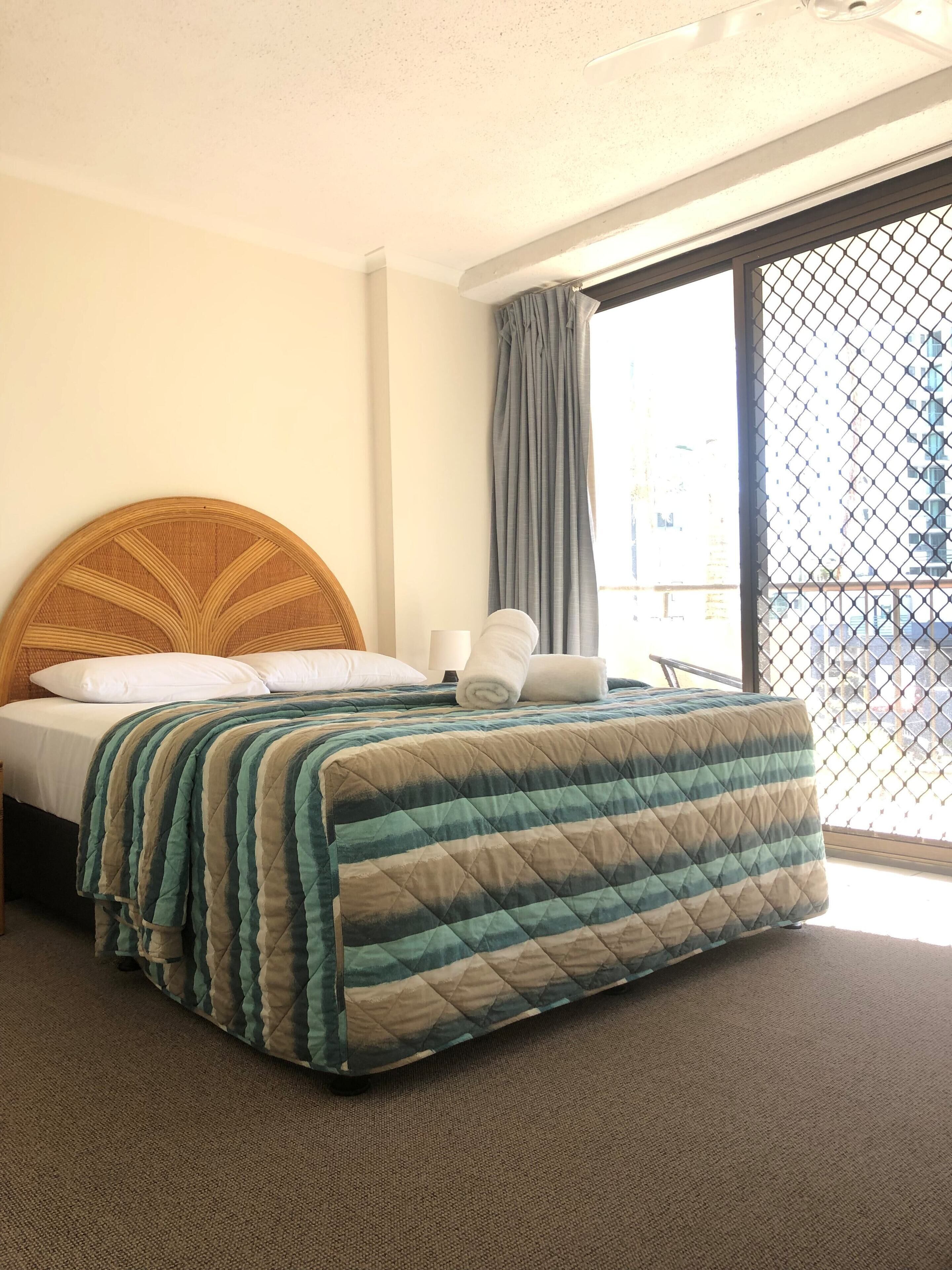 Una habitación de hotel con una cama, cabecera de madera, ventana con vistas y cortina.