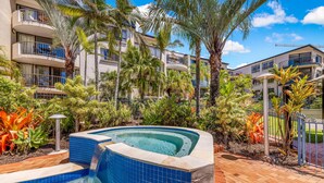 A hotel with a swimming pool surrounded by palm trees and tropical plants. - Kalua Holiday Apartments (Maroochydore)