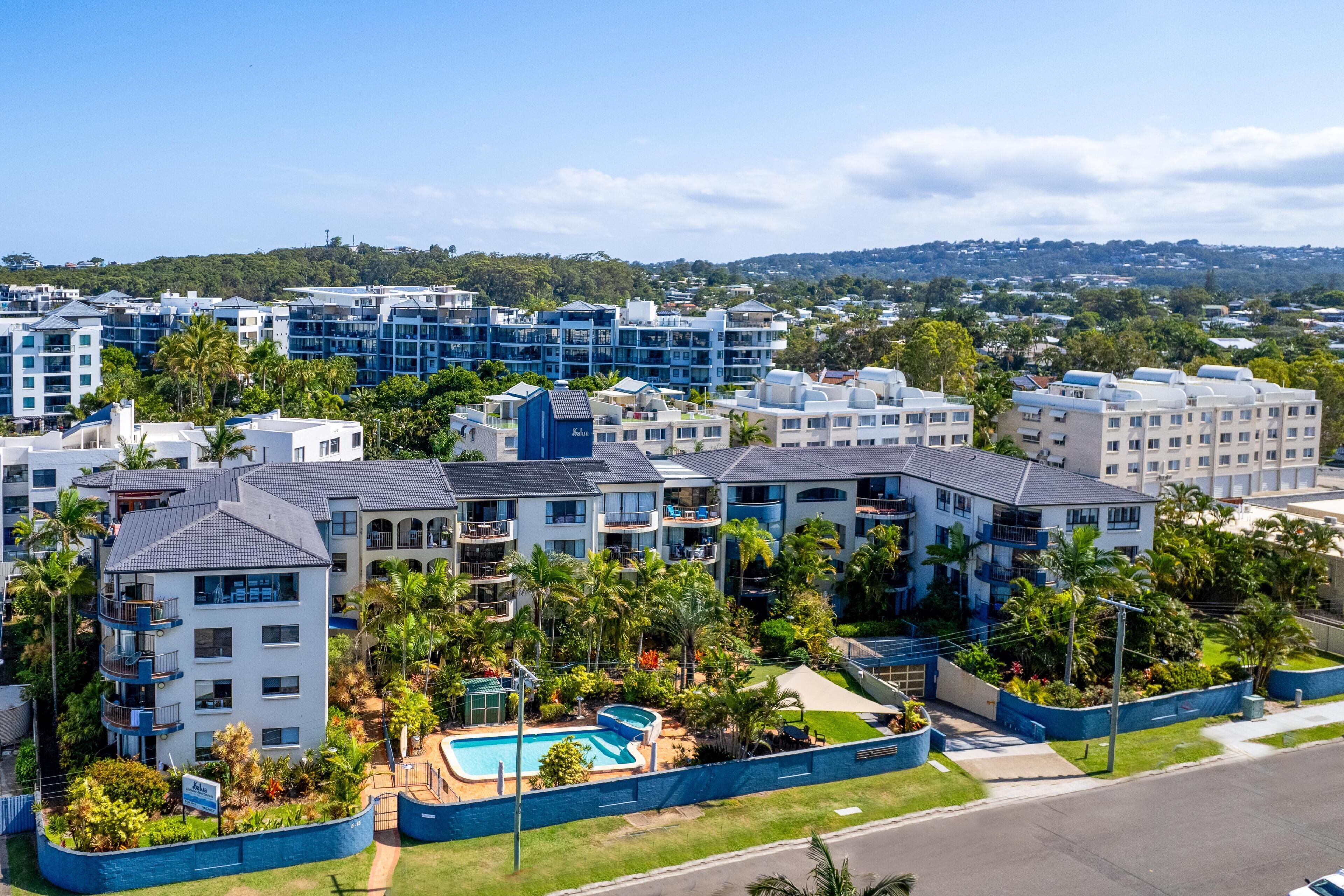 A residential complex with multiple apartment buildings, a swimming pool, and surrounding greenery.