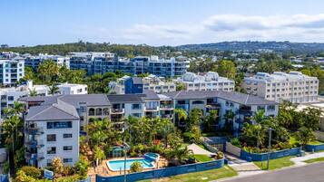 A residential complex with multiple apartment buildings, a swimming pool, and surrounding greenery.
