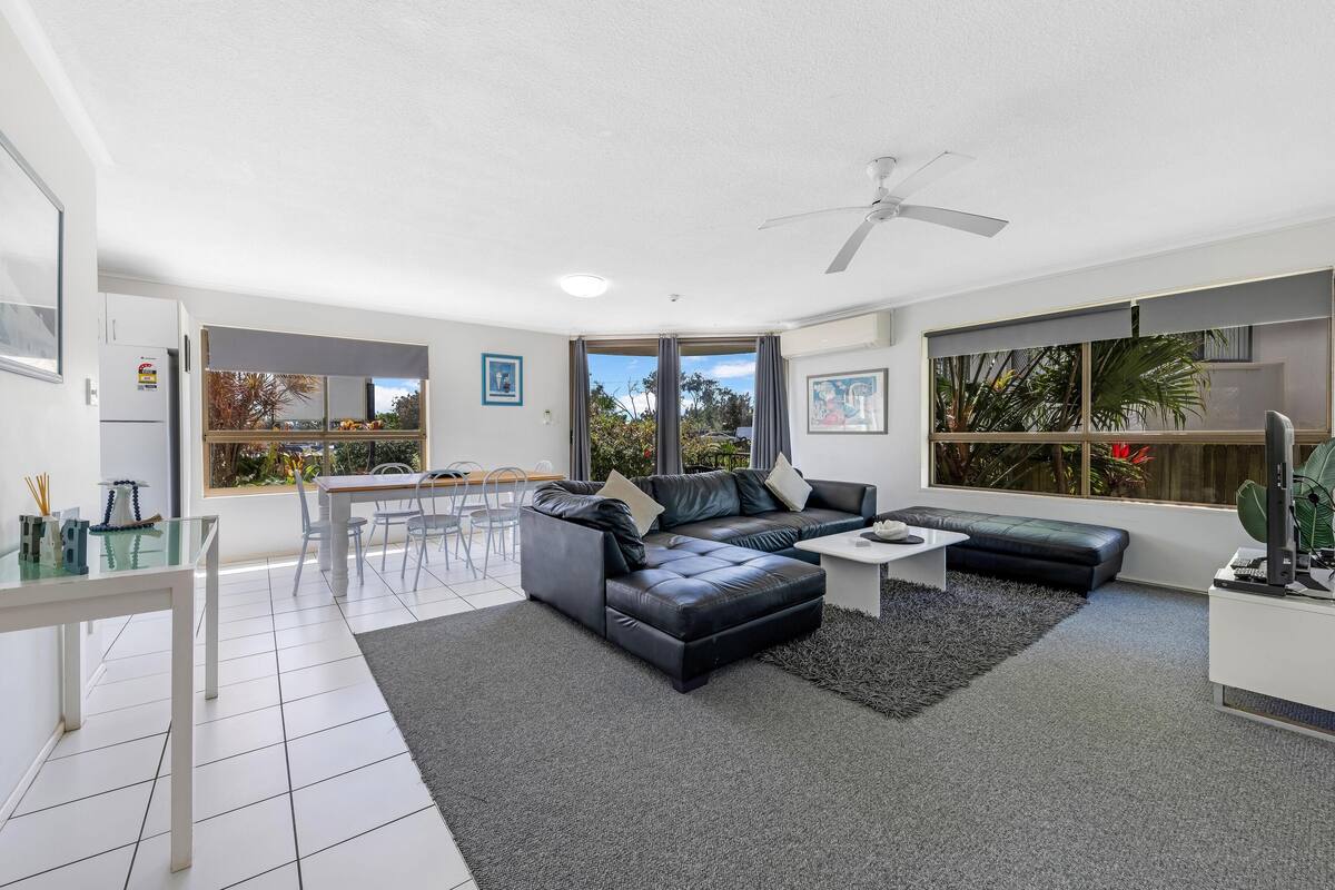 A modern living room with a black leather sofa, a glass dining table, and a ceiling fan.