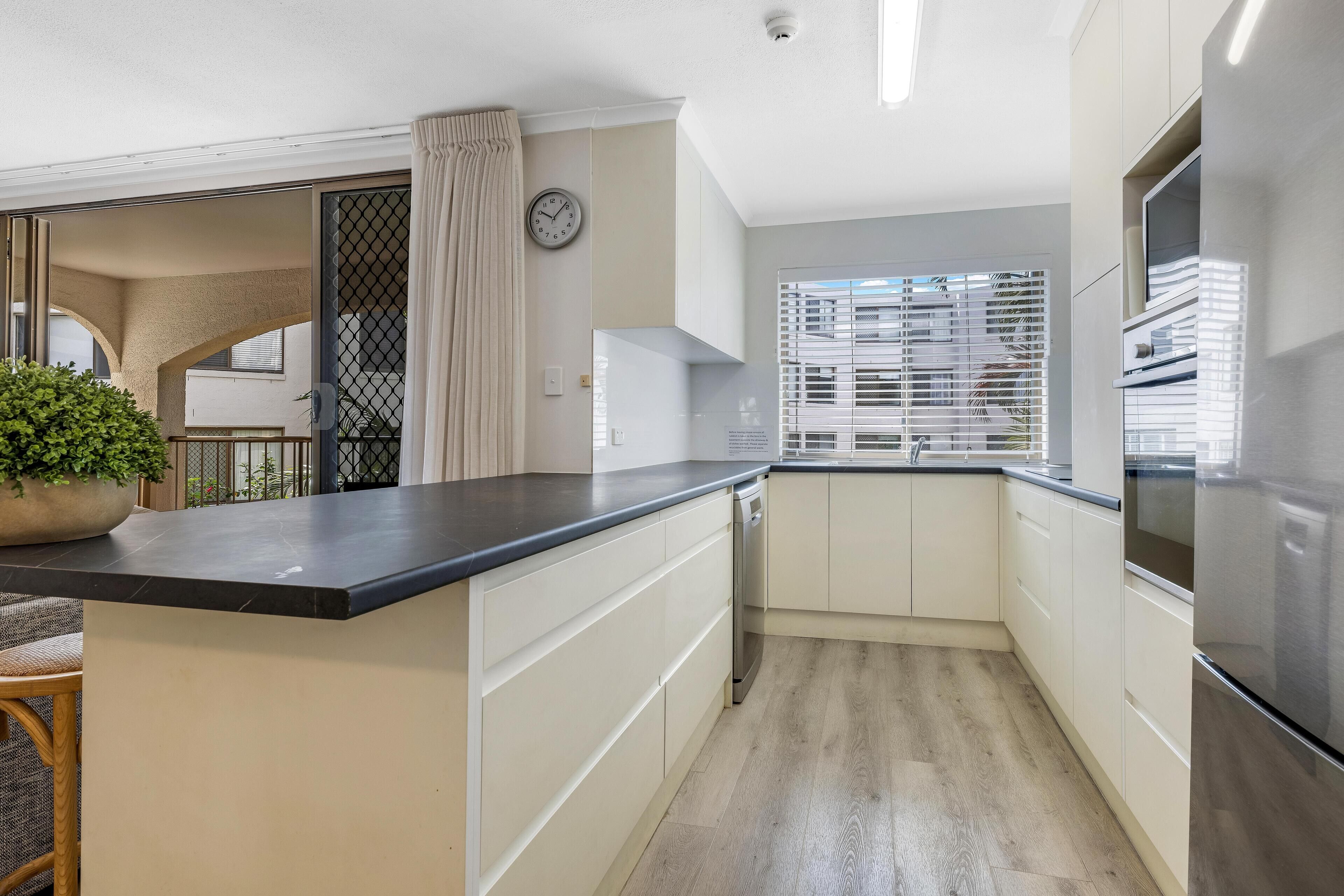 Een moderne keuken met een zwart aanrecht, witte kastjes en een roestvrijstalen koelkast.