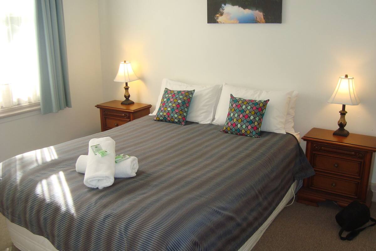 A neatly made bed with striped bedding, two bedside lamps, and a small wooden nightstand.
