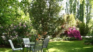 An outdoor seating area with a table and chairs, surrounded by lush greenery and flowering bushes. - Elm Lodge (Bright)