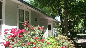 A house with a porch, surrounded by lush greenery and flowering plants. - Elm Lodge (Bright)