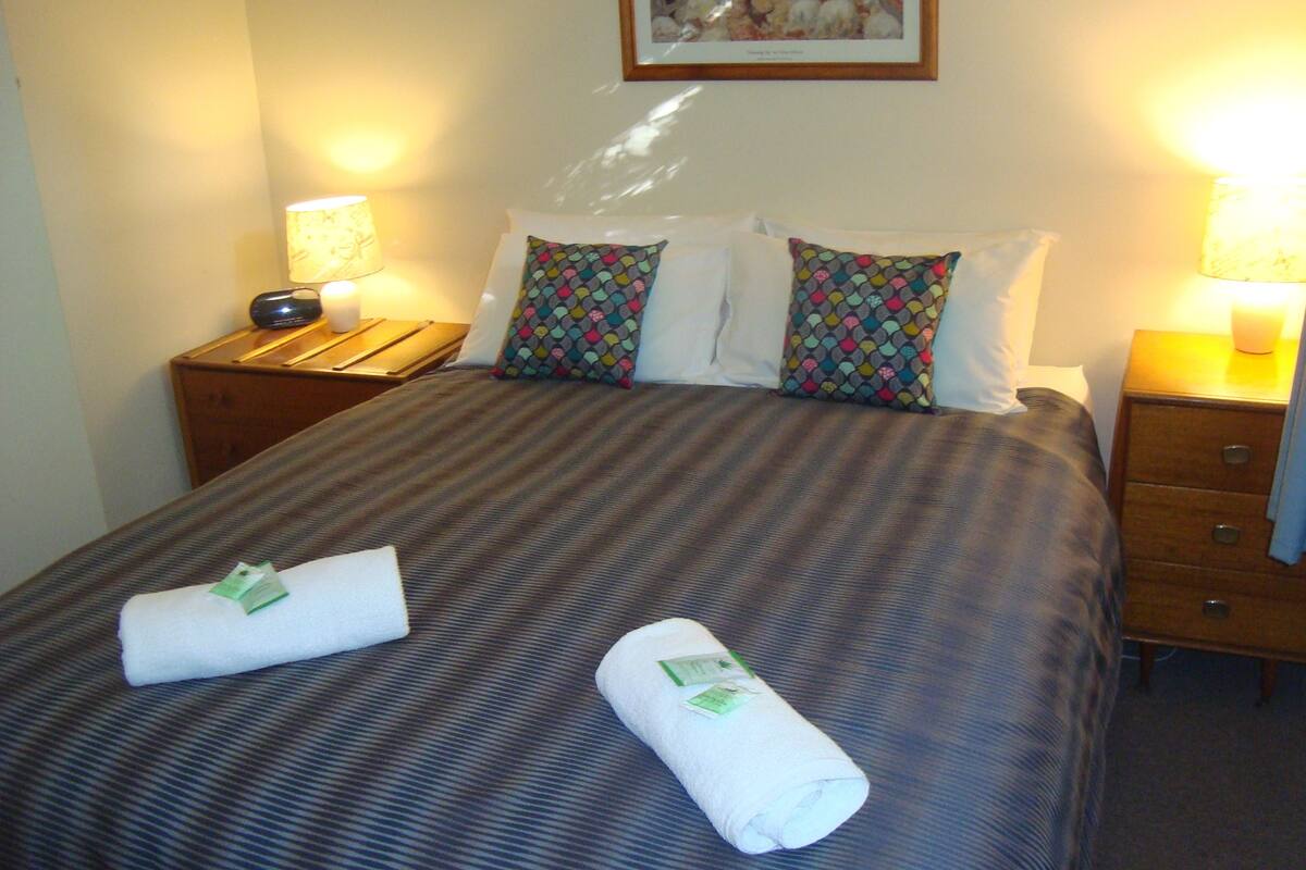 A hotel room with a neatly made bed, two bedside lamps, a wooden nightstand, and a framed picture on the wall.