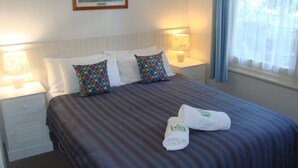 A neatly made bed with striped bedding, two decorative pillows, and two towels on the bed. - Elm Lodge (Bright)