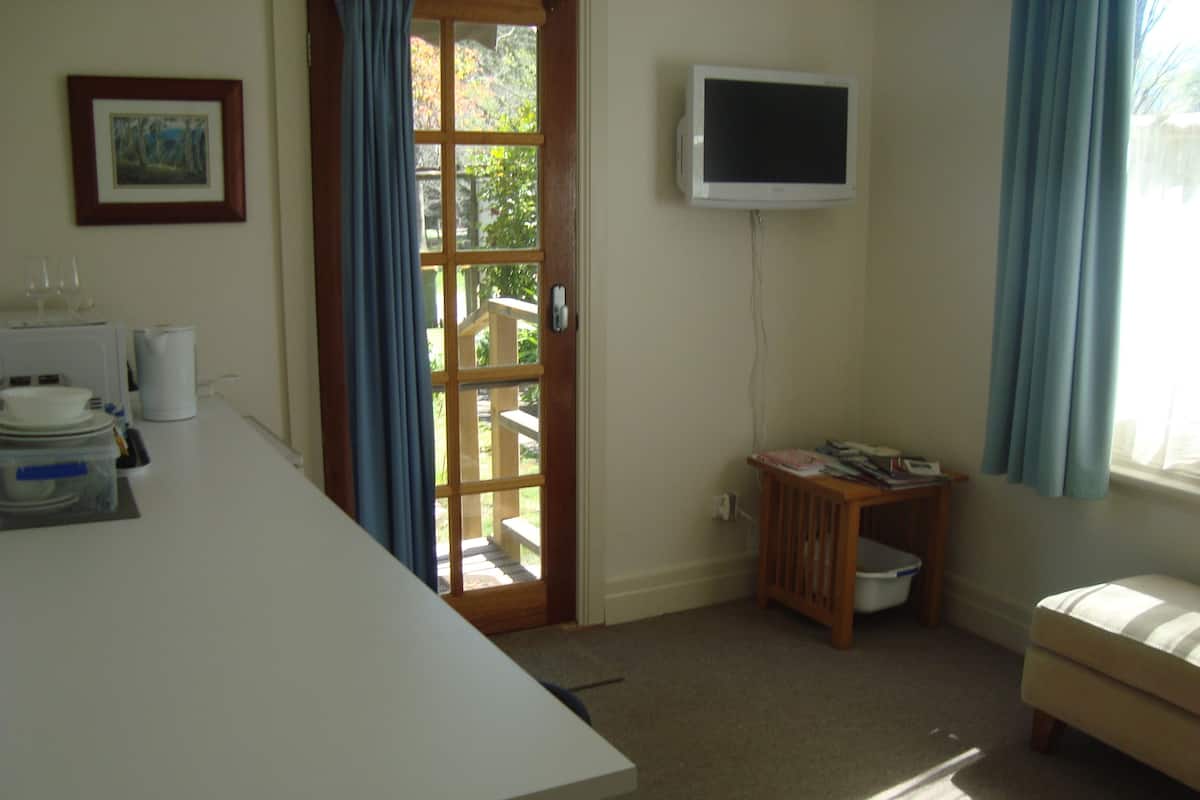 A room with a white table, a television mounted on the wall, a wooden bench, and a door leading to an outdoor area.