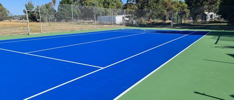 Una cancha de tenis exterior con superficie azul y zona verde circundante.