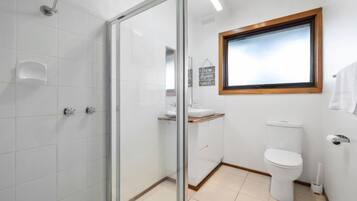 A bathroom with a glass shower enclosure, a white toilet, a sink with a wooden countertop, and a window with a wooden frame.