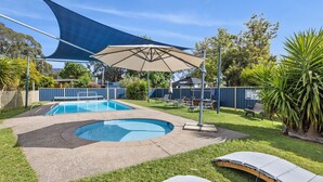 Piscina com área coberta, cadeiras de descanso e gramado com árvores.
