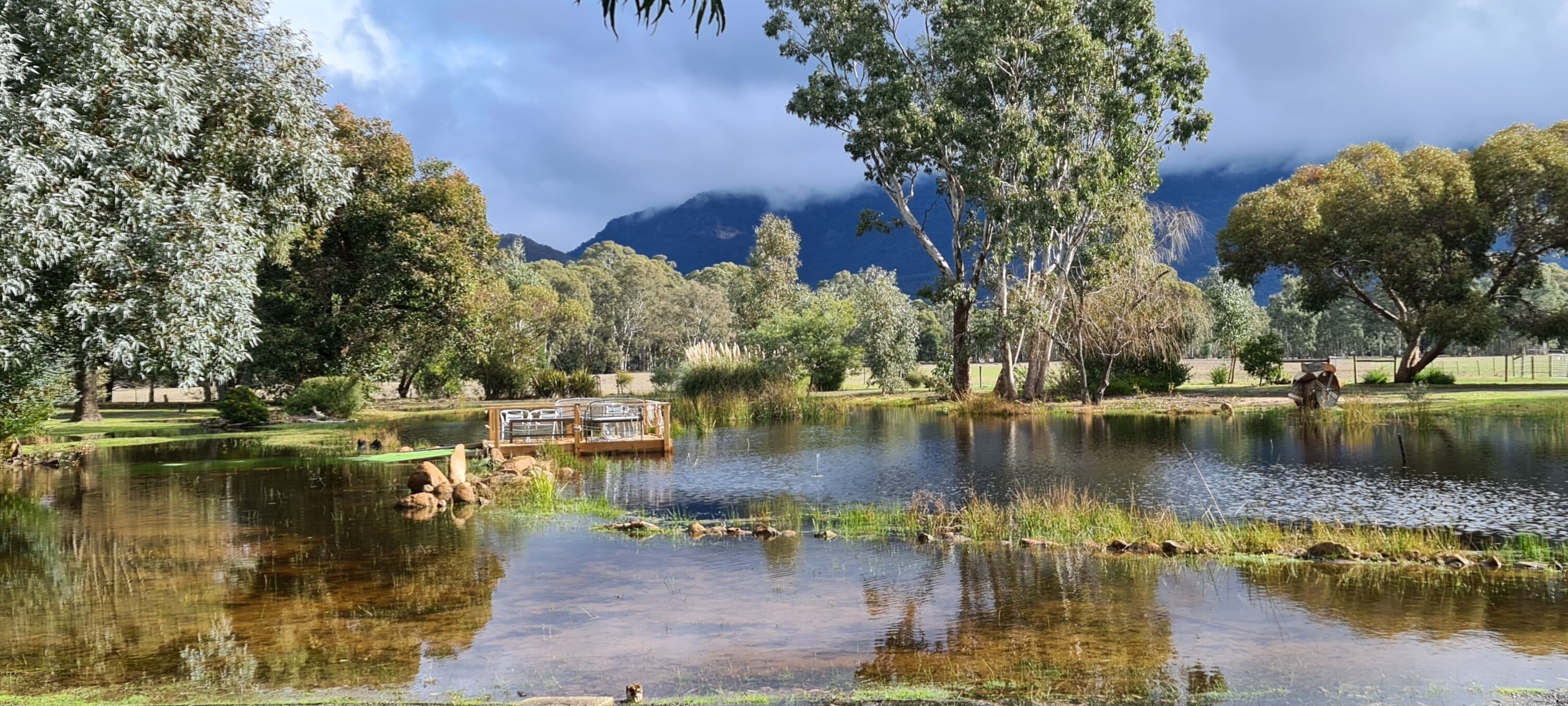 A serene lake with a wooden dock, surrounded by lush trees and a mountain backdrop.