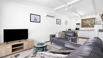 A modern living room with a flat-screen TV, leather sofa, and a dining area with a kitchen in the background.