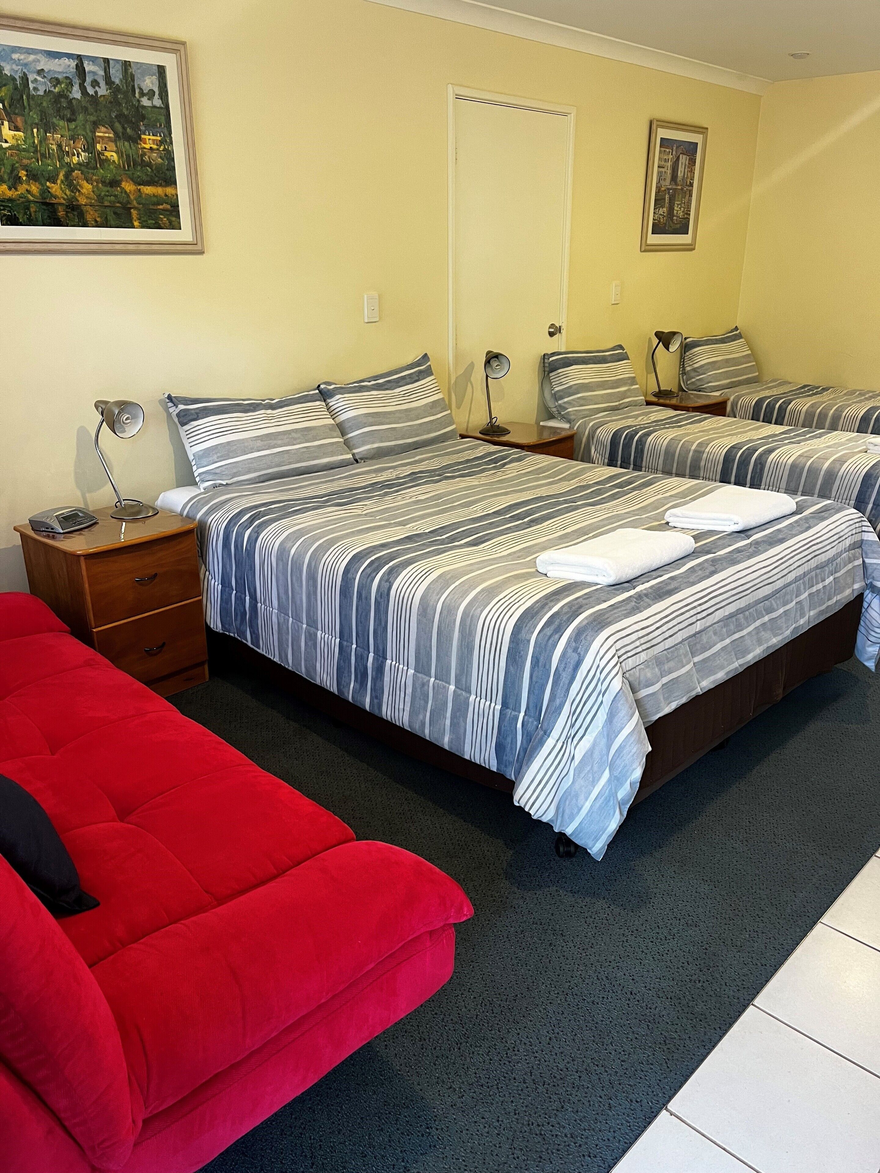 Une chambre d’hôtel avec deux lits, un canapé rouge et un tableau au mur.