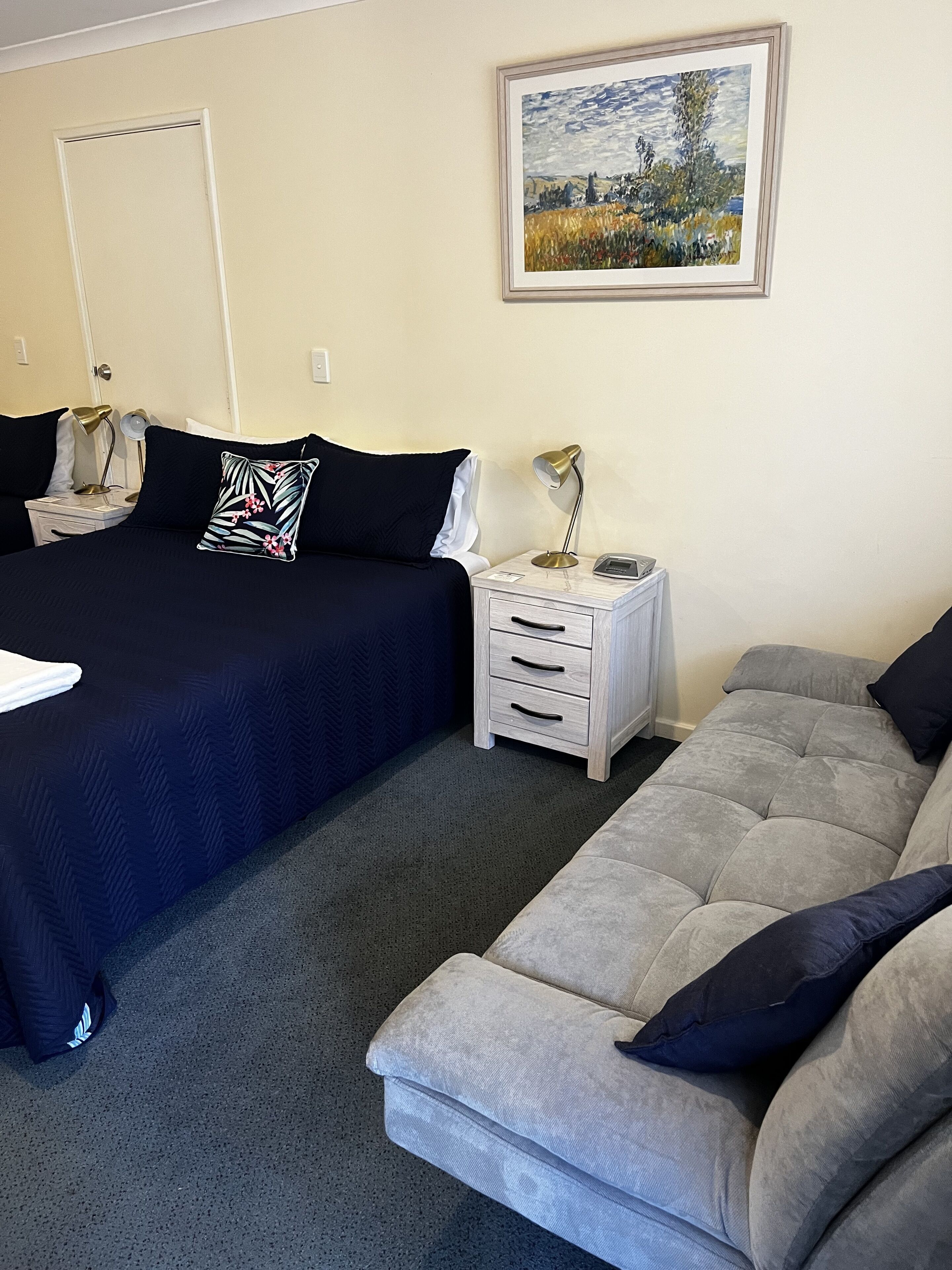 Un dormitorio con cama, mesitas de noche, lámpara, sofá y un cuadro en la pared.