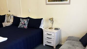 Un dormitorio con cama, mesitas de noche, lámpara, sofá y un cuadro en la pared.