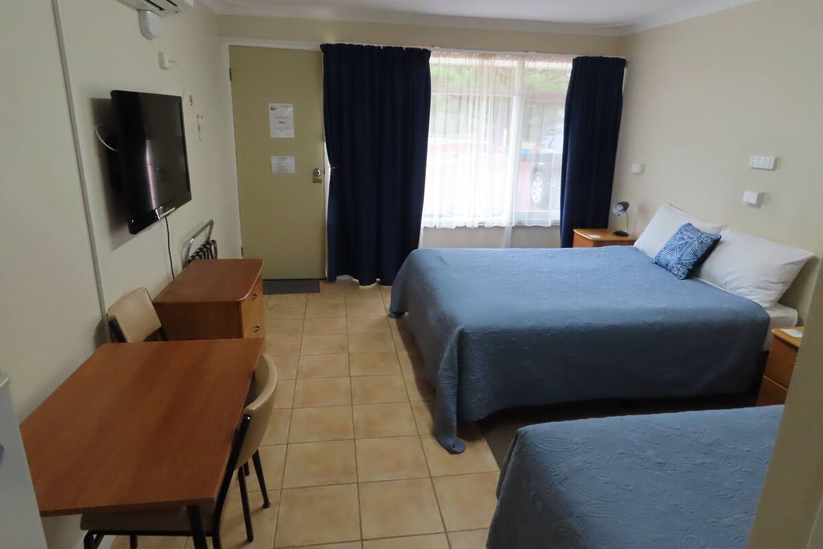 A hotel room with a bed, a desk, a chair, a TV, and a window with curtains.