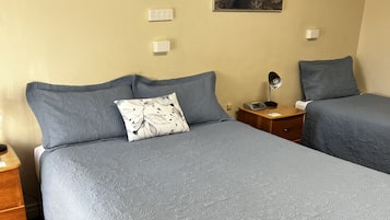 A double bed with a floral-patterned pillow, a nightstand with a lamp, and a wall-mounted power outlet.