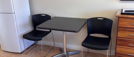 Una habitación compacta con kitchenette, una mesa de comedor con dos sillas, un sofá rojo y un televisor en la pared.