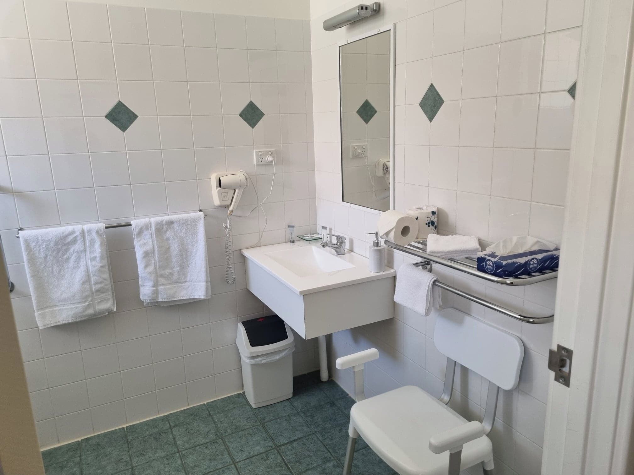 A bathroom with white tiles, a sink, a mirror, a towel rack, a trash bin, and a toilet.