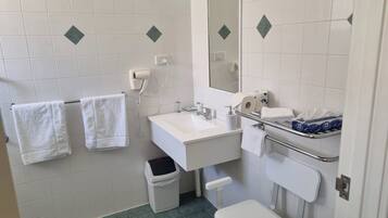 A bathroom with white tiles, a sink, a mirror, a towel rack, a trash bin, and a toilet.