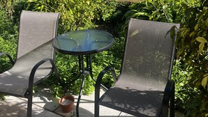 An outdoor seating area with two chairs and a table, surrounded by lush greenery and trees. - Emu Point Motel & Apartments (Emu Point)