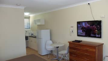 A compact room with a kitchenette, a small dining table with two chairs, a wooden dresser, and a television mounted on the wall.
