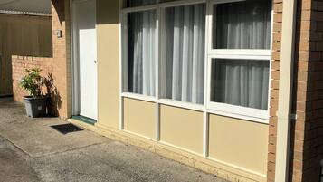 A single-story building with a beige exterior, a white door, and a large window with curtains.